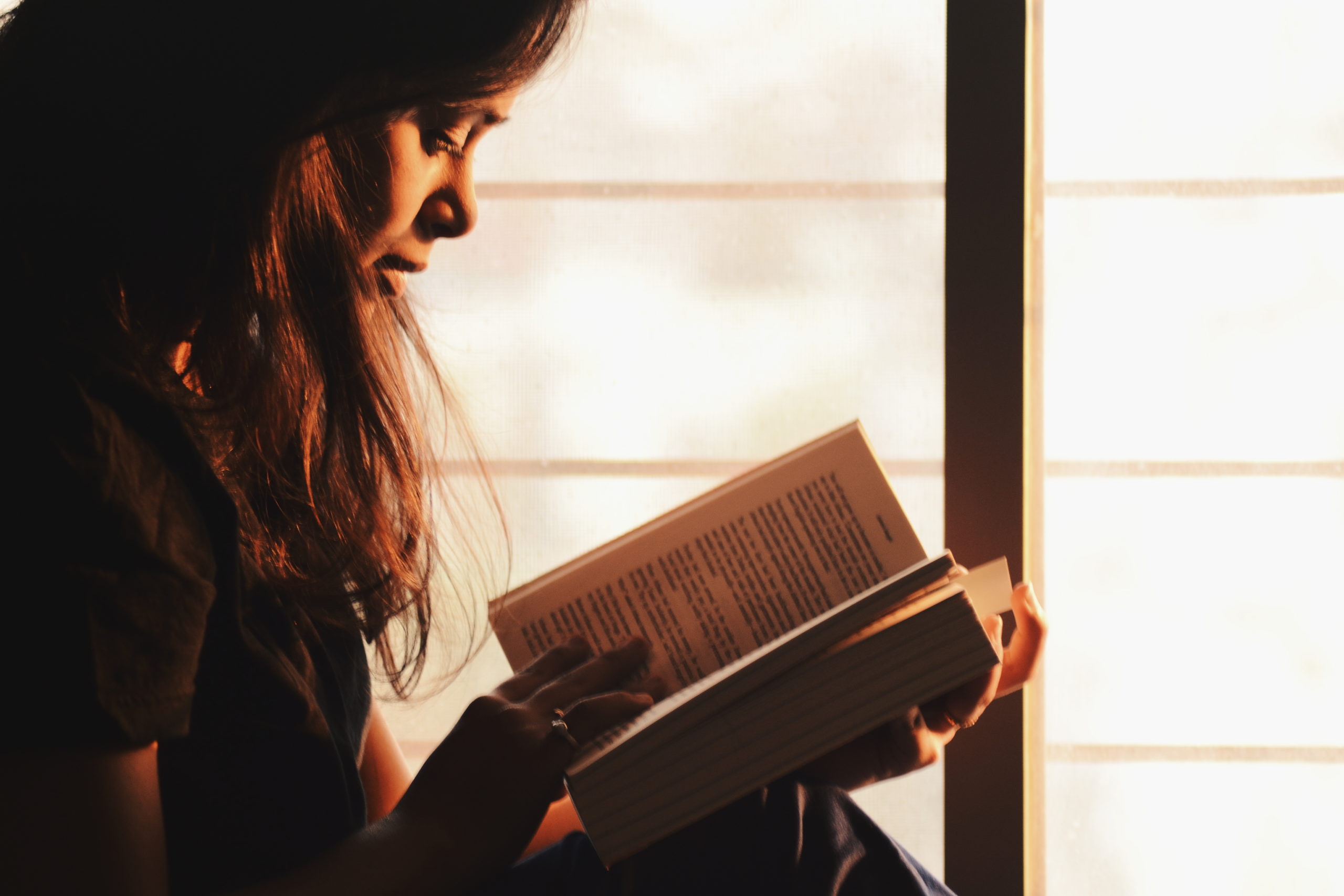 woman reading a book beside the window 1031588 scaled